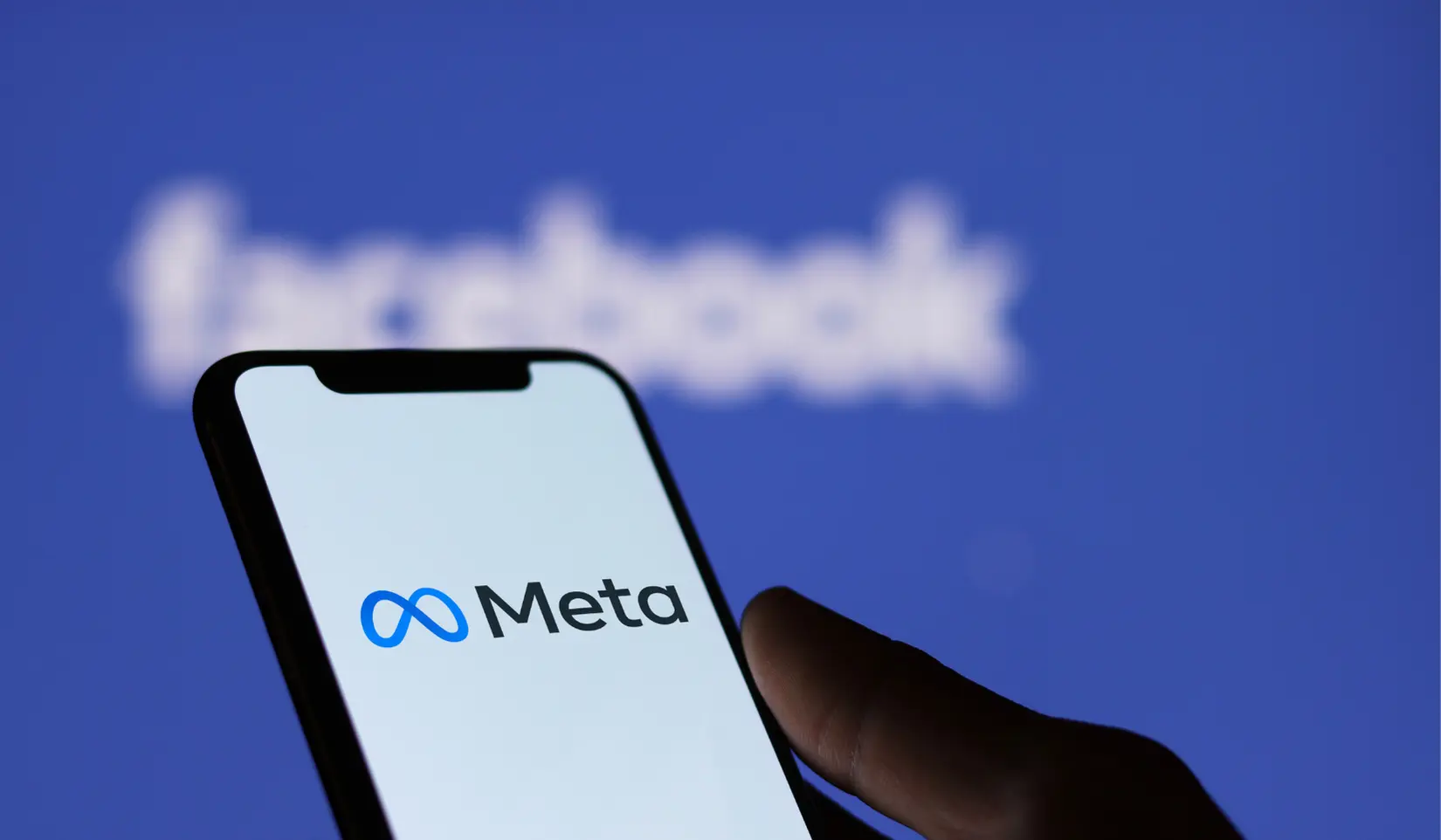 Smartphone displaying the Meta logo in front of a Facebook sign